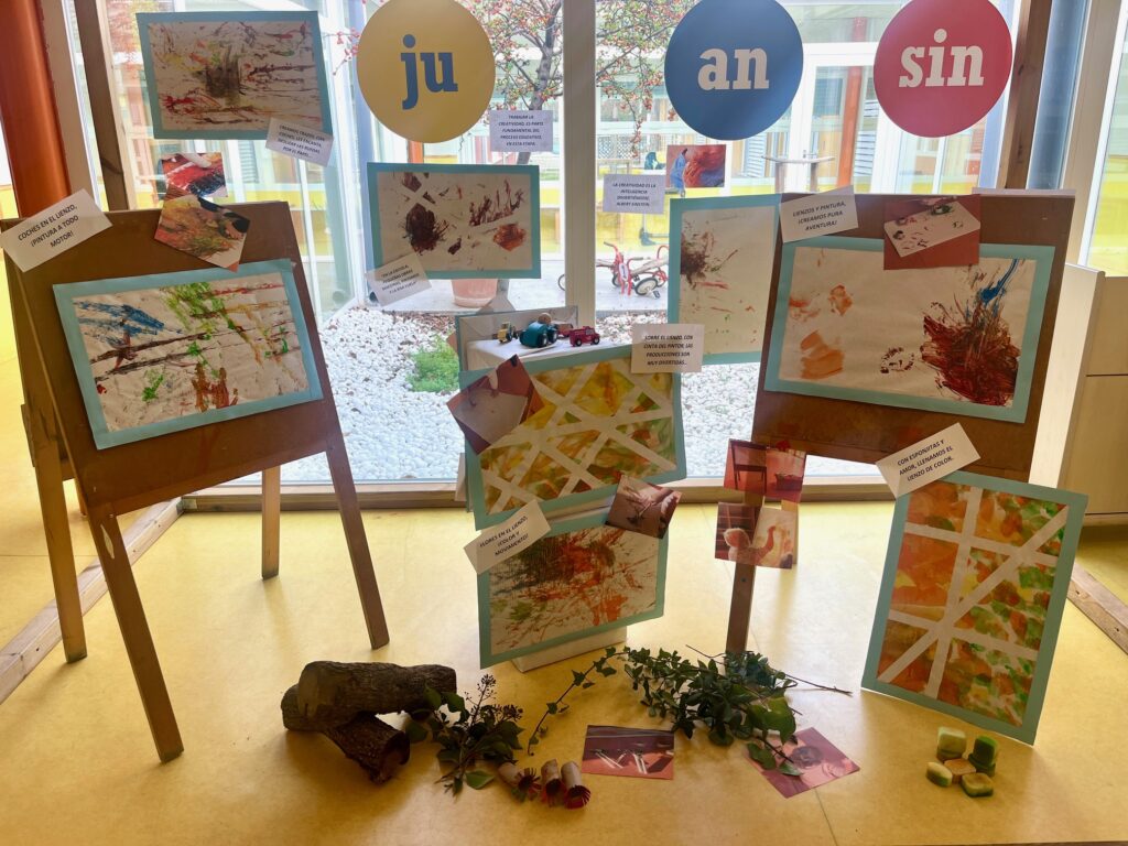 Galería de arte infantil con lienzos coloridos expuestos en caballetes de madera en la Escuela Juan sin Miedo.