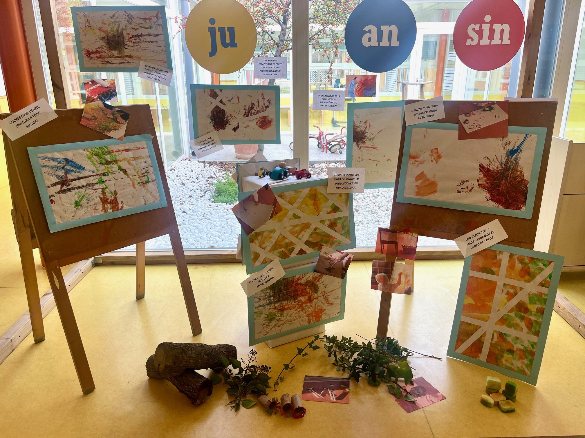 Galería de arte infantil con lienzos coloridos expuestos en caballetes de madera en la Escuela Juan sin Miedo.