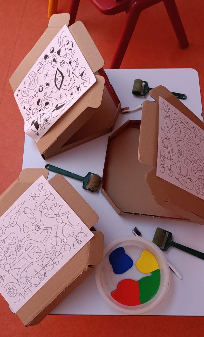 Cajas de cartón con láminas de Miró, rodillos de pintura y paleta con colores primarios (rojo, azul, amarillo y verde).