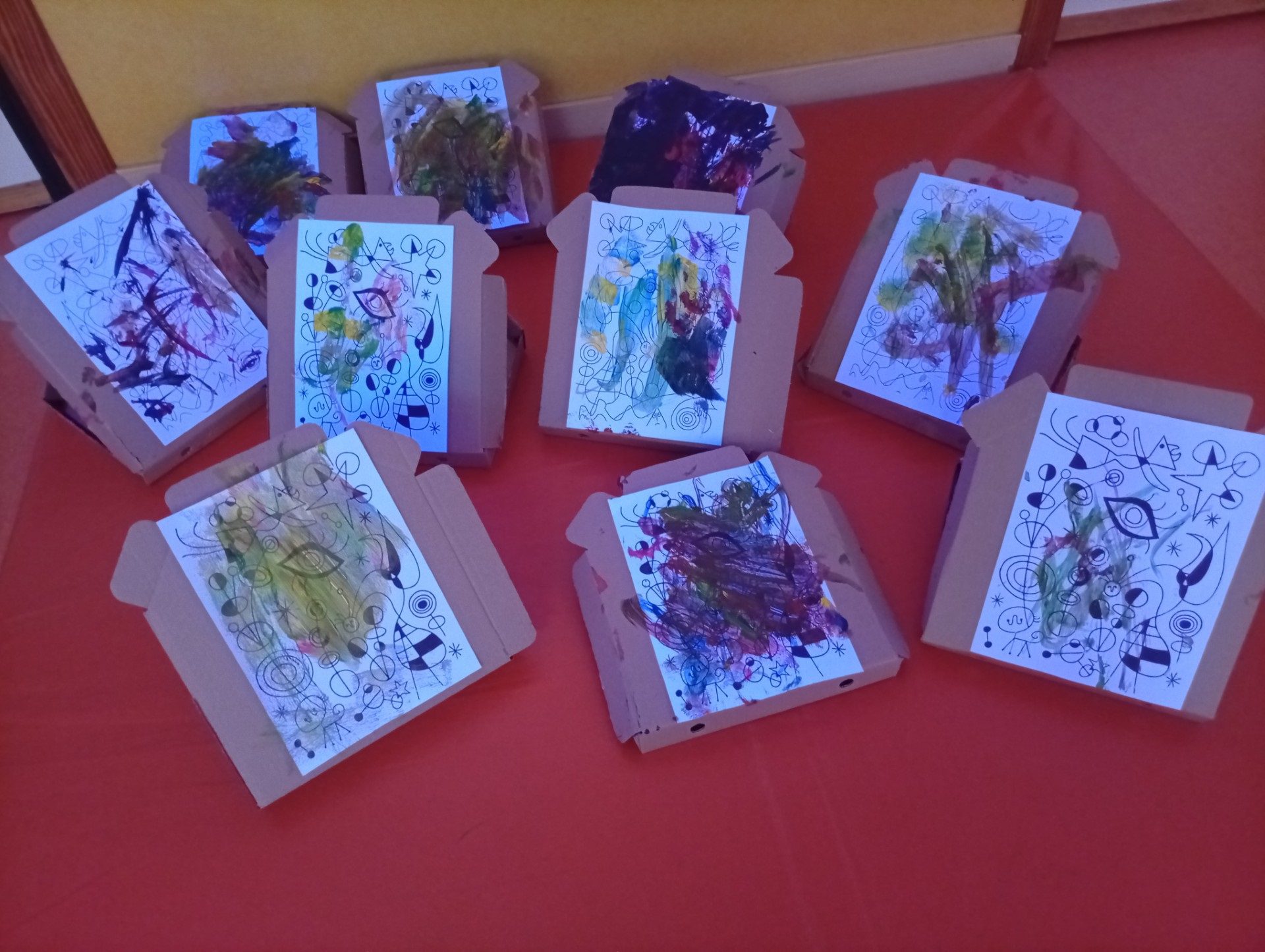 Exposición de trabajos artísticos infantiles con trazos libres y colores sobre láminas geométricas.